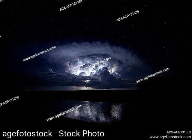 Storm with cloud lightning flashing over pond in rural Kansas, United States