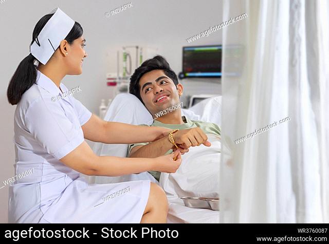 NURSE IN THE ROLE OF A SISTER TYING RAKHI TO THE BOY ADMITTED IN THE HOSPITAL