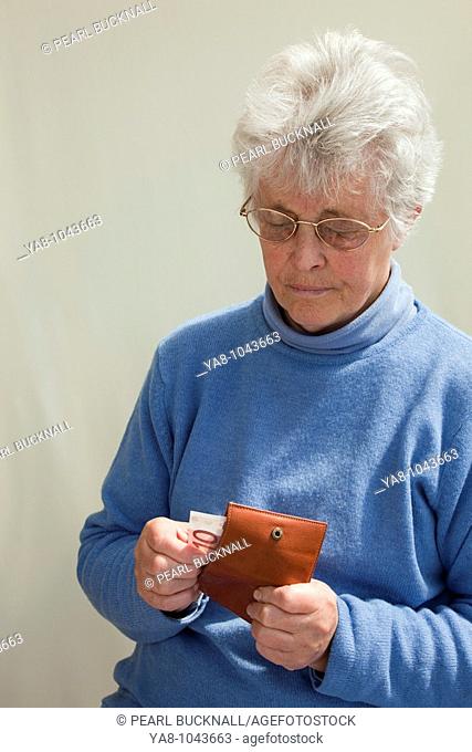 Europe  Senior woman pulling ten Euro note from a purse looking worried MR 09/05