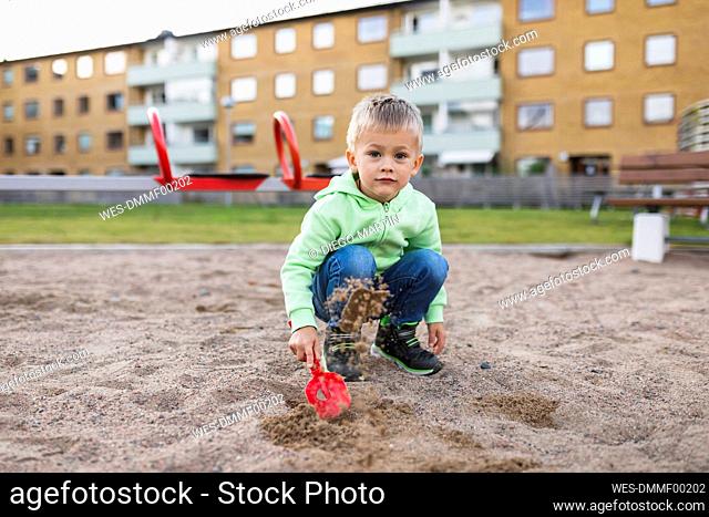 Cute boy splashing sand with shovel in playground