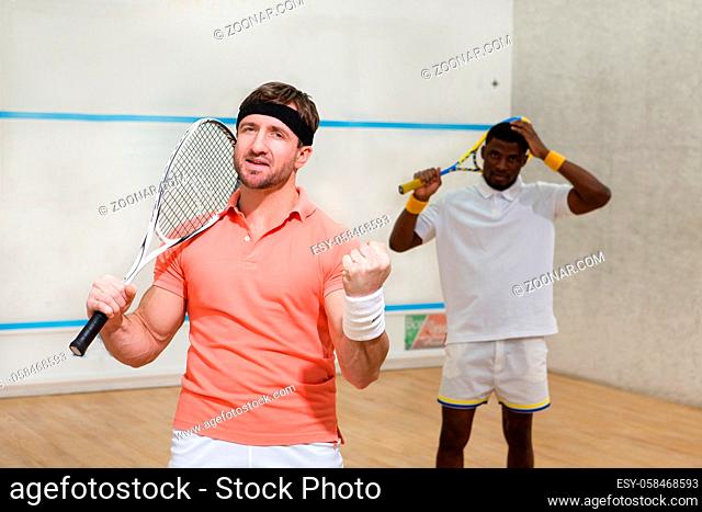 Handsome men playing squash on court and expressing positive emotions during game: excitedness, astonishmen