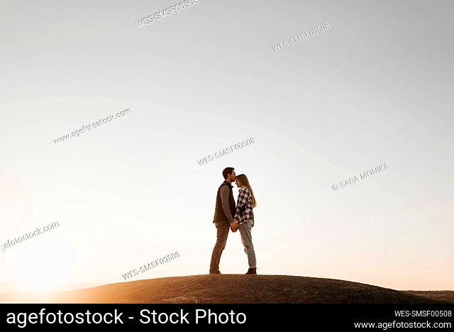 Young couple holding hands against clear sky at sunset