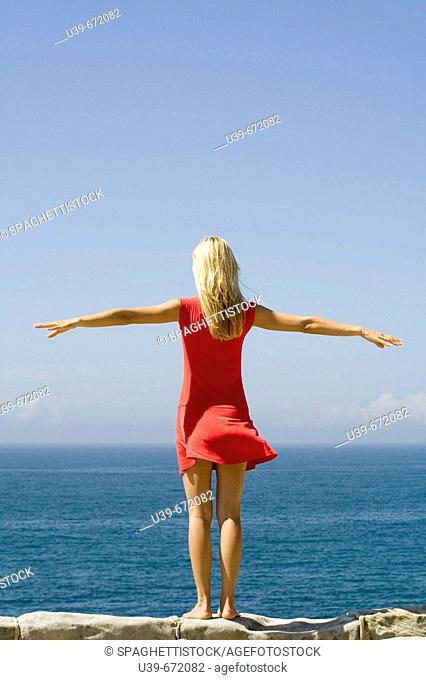 Woman standing on a wall overlooking the sea. Shot from behind. Sydney, Australia