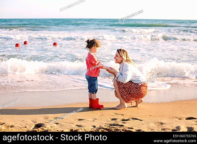 Young loving mother with smiling daughter running towards her on sunny beach, happy mom hug little girl, enjoying spending time together on summer seaside