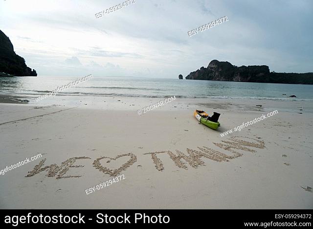 We love Thailand - text written by hand in sand on a sea beach with kayak over sky