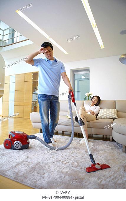 Woman On Couch Listening Music And Man Vacuuming