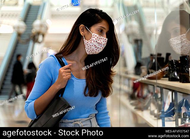 Beautiful woman wearing protective face mask while looking at footwear in shopping mall