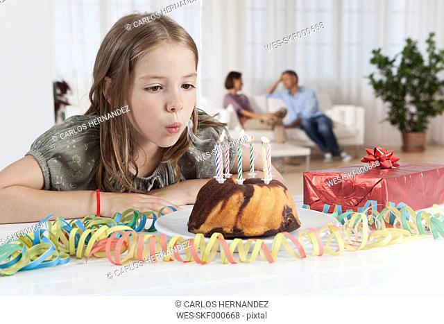 Germany, Munich, Girl blowing candles of birthday cake, parents in background