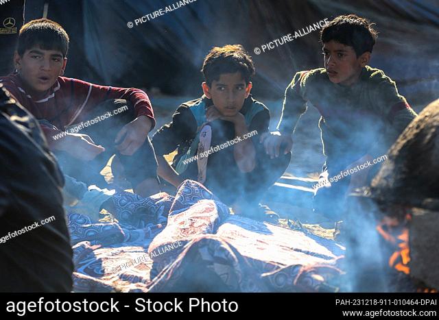 18 December 2023, Palestinian Territories, Rafah: Children look on as people gather around clay ovens to reserve their turn to prepare food and bake bread