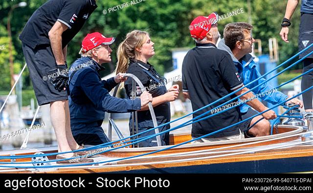 26 July 2023, Schleswig-Holstein, Lübeck-Travemünde: Schleswig-Holstein's Minister President Daniel Günther (CDU, l) steers the 12-man sailing yacht Sphinx to...