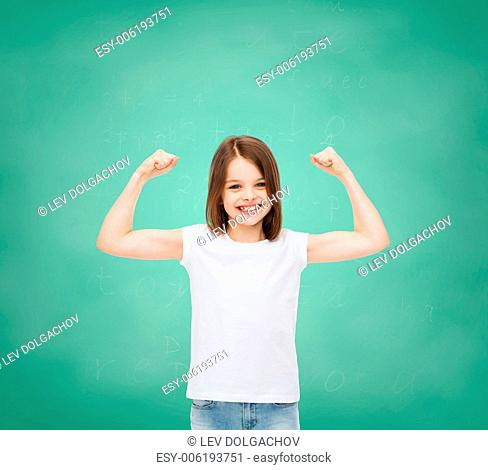 advertising, gesture, school, education and people - smiling little girl in white blank t-shirt with raised arms over green board background