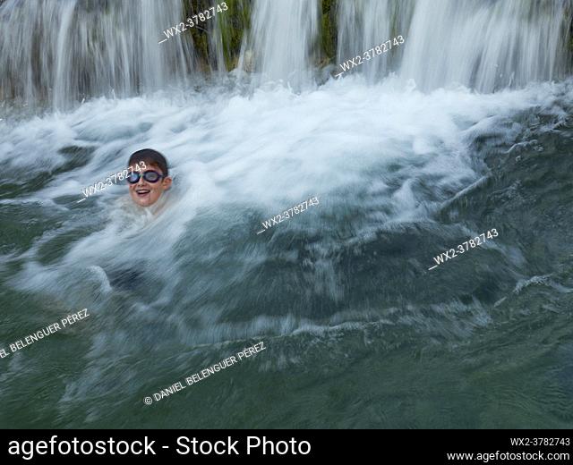 Boy swimming and laughing on a waterfall in a mountain river. Villahermosa river, Ludiente, Castellón, Spain