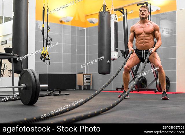 Muscular powerful man working out with rope in functional training fitness gym. High quality photo