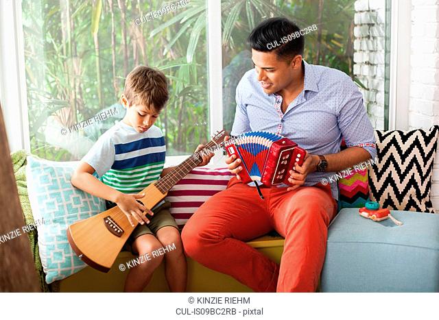 Boy playing guitar with music teacher on window seat