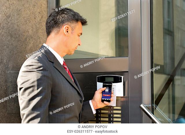 Mature Businessman Holding Smartphone For Disarming Security System Of Door