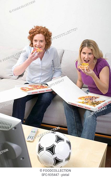 Two friends eating pizza while watching TV