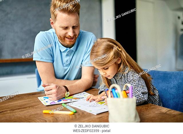 Father and daughter sitting at table, painting colouring book