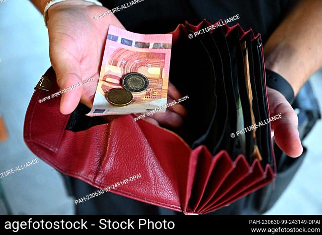 30 June 2023, Bavaria, Munich: A waiter at a restaurant is holding a wallet in his hand while holding money in the other hand
