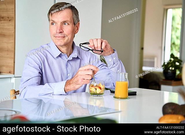 Middle-aged professional man having breakfast on kitchen counter at home