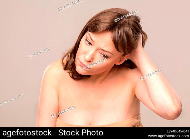 Upset beautiful woman looking down and touching her middle length hair. White studio shooting. Mid age woman over 35 years old concept