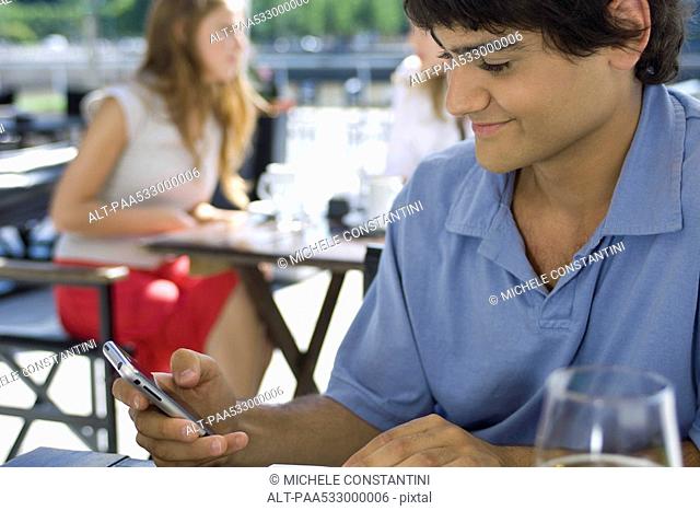 Young man sitting at outdoor cafe, using cell phone