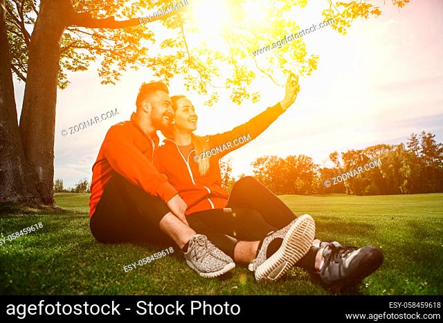 Sport man and woman making selfies in green park or forest while resting and relaxing after hard-working day. Fitness, sportrs and lifestyle concepts