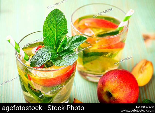 Cold fresh lemonade drink with, nectarine, lime and mint on a green wooden background