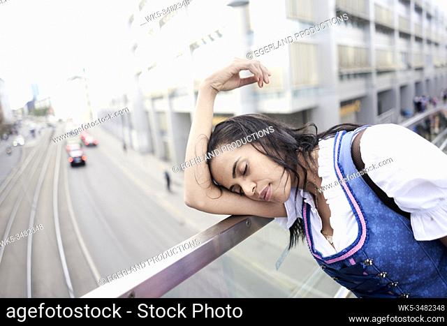 Brazilian woman wearing Dirndl, leaning on railing, exhausted. Munich, Germany