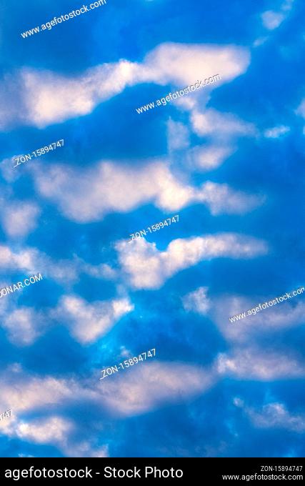 Dramatic clouds in blue sky, illuminated by rays of sun at sunset to change weather. Soft focus, motion blur multicolored cloudscape abstract background