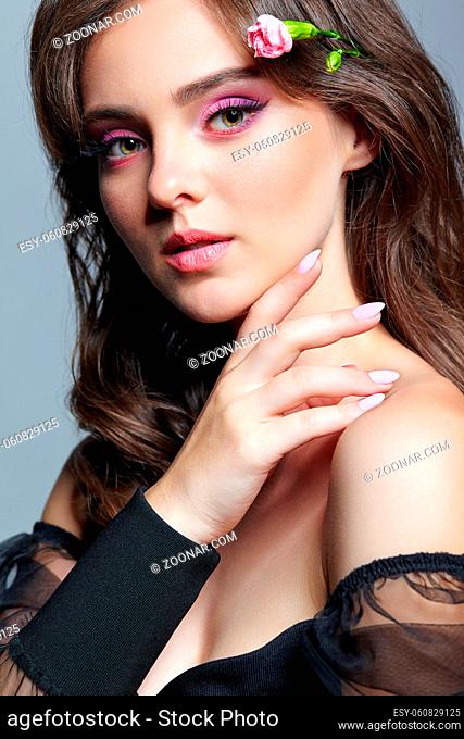 Beauty portrait of young woman with hand near face. Brunette girl with evening female makeup and black dress. Pink carnation flower in hairs