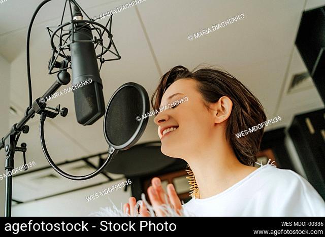 Smiling singer recording music through microphone in studio