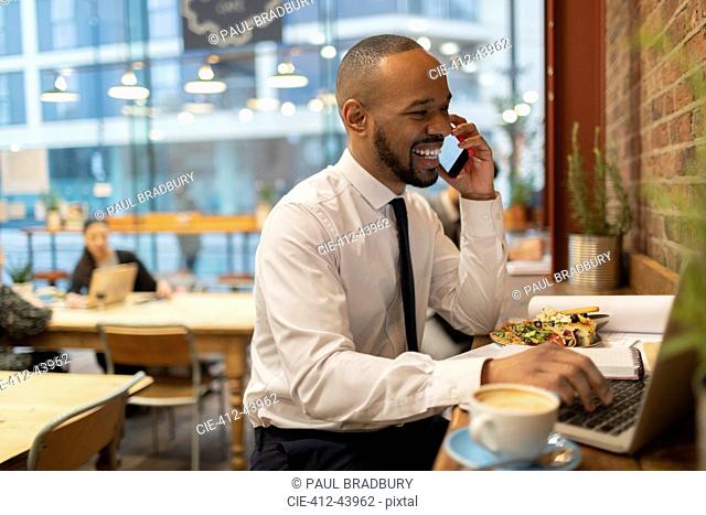 Smiling businessman talking on smart phone, working in cafe