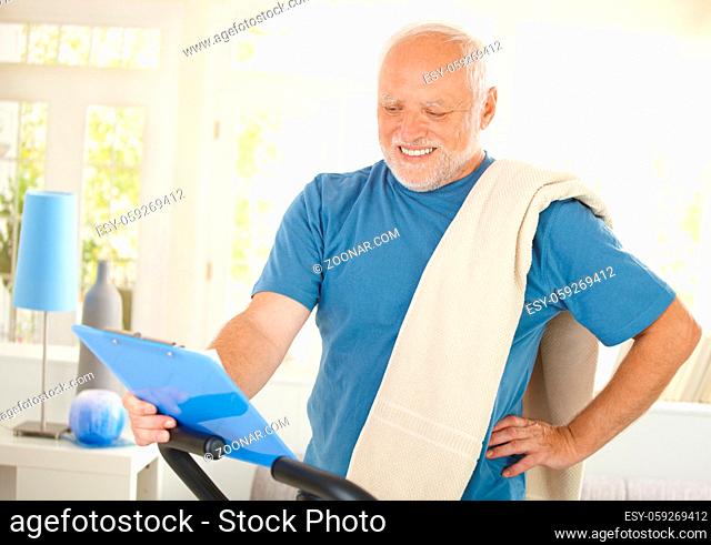 Happy senior man in sportswear looking at clipboard at home