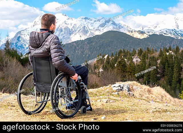 Photo of Young disabled man in wheelchair outside in nature observing mountains and nature
