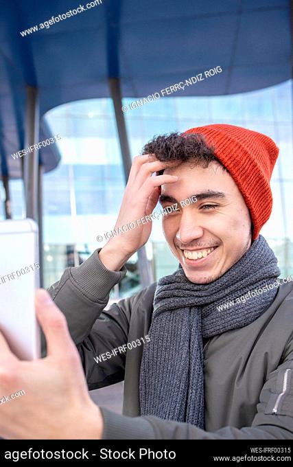 Smiling man with hand in hair taking selfie in city
