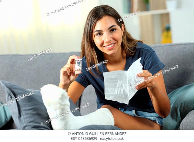 Happy disabled woman showing a bottle of pills sitting on a couch in the living room at home