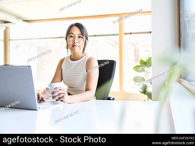Smiling businesswoman with coffee cup sitting at desk