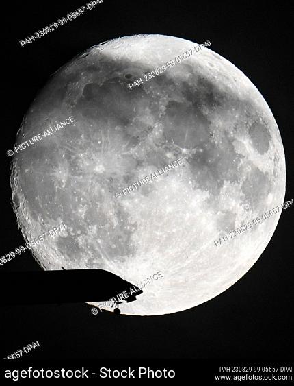 29 August 2023, Hesse, Frankfurt/Main: A passenger plane is on approach to Frankfurt Airport while the moon shines in the evening sky