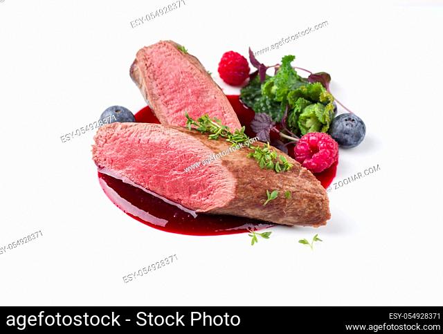 Fried dry aged venison tenderloin fillet medallion steak natural with kalette and raspberry sauce as closeup on a modern design plate