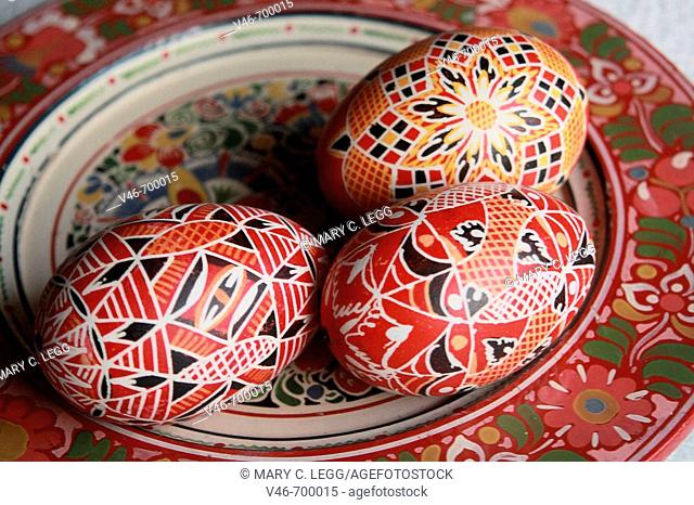 three red traditional Czech Easter eggs rest on a handpainted wooden Bohemian plate. The eggs have tradtional red geometrical design that is very popular