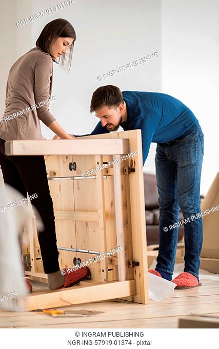 Happy young couple putting together self assembly furniture as they move into their new house