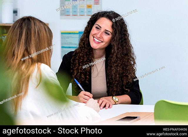 Smiling businesswoman at desk looking at woman in office