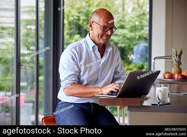 Smiling man using laptop at kitchen island