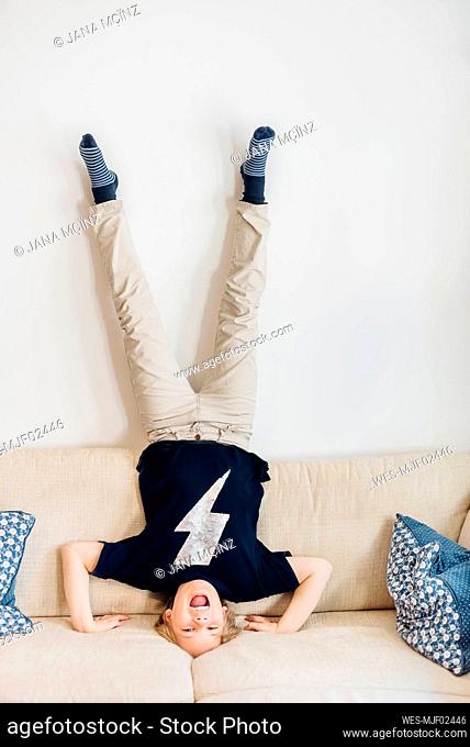 Carefree boy doing a headstand on couch in living room at home