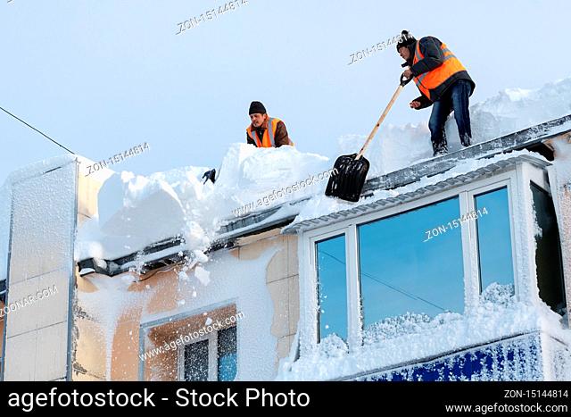 PETROPAVLOVSK CITY, KAMCHATKA PENINSULA, RUSSIA - DEC 27, 2017: Workers in orange vests with snow shovels cleaning snow drifts from roof of multistory building...