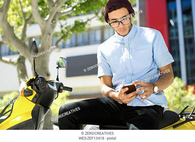 Young man sitting on motor scooter using cell phone