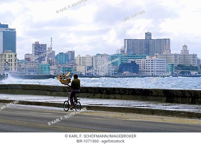 Man transporting a small model ship on a bike, Malecon quay, view of modern Vedado district, Havana, Cuba, Caribbean