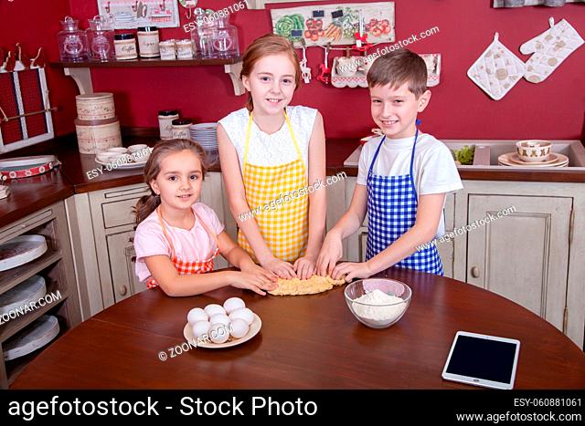 Children in the kitchen trying to learn cooking. Best friends in aprons holding pastry in their hands and making cake in kitchen and looking at each other