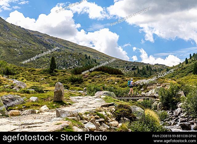 17 August 2023, Austria, -: A woman walks across a bridge on a hiking trail between Tyrol (Austria) and South Tyrol (Italy)
