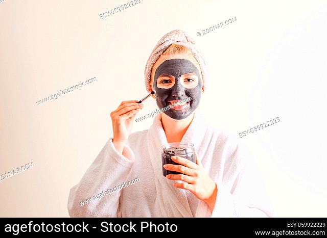 Smiling woman in a towel on the head applying black nourishing mask on face at home